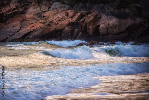 Sunlit waves rolling against a backdrop of rock.