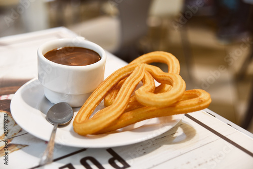 Traditional Spanish dessert churos with hot spicy chocolate and sugar in a pan on a wooden table, selective focus photo