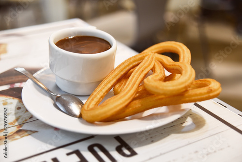 Traditional Spanish dessert churos with hot spicy chocolate and sugar in a pan on a wooden table, selective focus