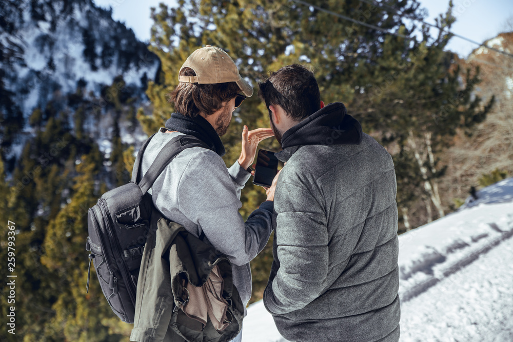 Back view of young photographers with professional camera and mobile phone standing between mountains in snow in Cerdanya, France Back view of young photographers with professional camera and mobile phone standing between mountains in snow in Cerdanya, France