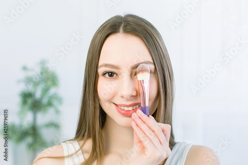 Portrait of beautiful young Caucasian woman with clean face. Beauty spa model girl with perfect fresh clean skin applying cosmetic brush. Youth and skin care concept.