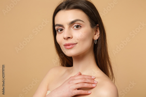 Close up brunette half naked woman 20s with perfect skin hand on shoulder isolated on beige pastel wall background studio portrait. Skin care healthcare cosmetic procedures concept. Mock up copy space