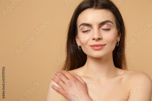 Close up brunette half naked woman 20s with perfect skin hand on shoulder isolated on beige pastel wall background studio portrait. Skin care healthcare cosmetic procedures concept. Mock up copy space