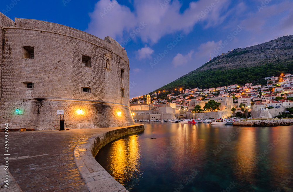 Sightseeing of Croatia. Dubrovnik old town, night view. The fortress wall and the port with boats, Croatia
