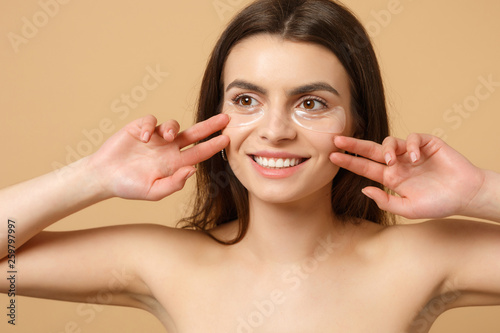 Close up half naked woman 20s with perfect skin  nude make up patches under eyes isolated on beige pastel wall background  studio portrait. Health care cosmetic procedures concept. Mock up copy space.