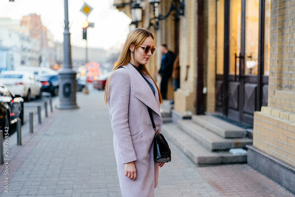 Beautiful young caucasian woman walking along the store fronts in the city. Stylish female model wearing sunglasses looking at store fronts on city street.
