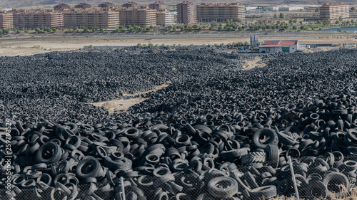 Huge pile of old auto tires between meadow near town and cloudy sky in sunny day photo