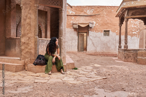 Young lady sitting near retro building on street in Marrakesh, Morocco photo