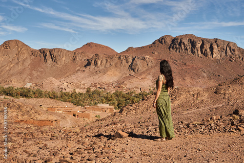 Back view of young brunette lady standing between desert lands near ancient constructions and hills in Marrakesh, Morocco photo