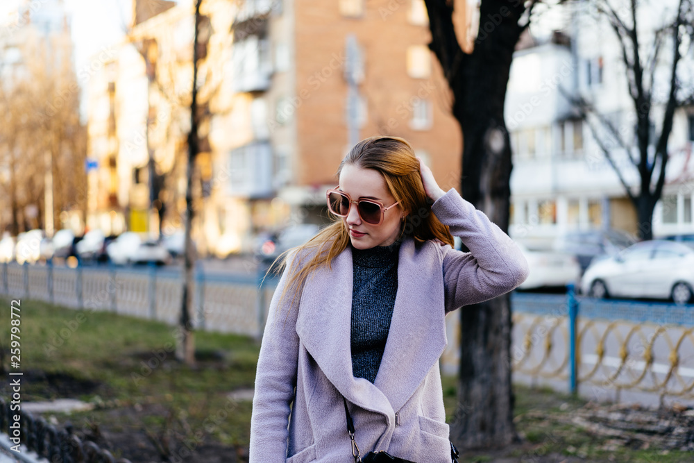 Beautiful young caucasian woman walking along the street in the city. Stylish female model running her hands through hair walking on city street. Beautiful young caucasian woman walking along the street in the city. Stylish female model running her hands through hair walking on city street.