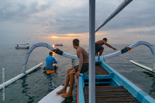 Side view of males jumping from shallop in waving sea and cloudy sky in evening on Bali, Indonesia