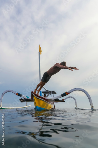 Side view of male jumping from shallop in waving sea and cloudy sky on Bali, Indonesia