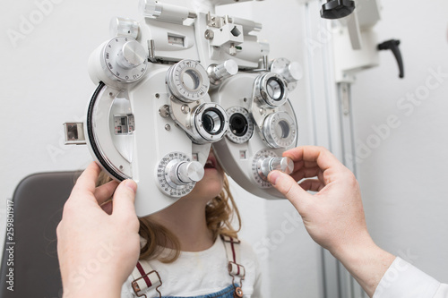 Optician testing a girl's eyes with optometry devices photo