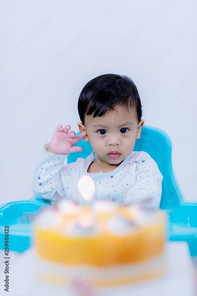 Cute little boy with birthday cake sitting on chair in room . mother holding birthday cake with candle in front of baby sitting in high chair . Cute little boy with birthday cake sitting on chair in room . mother holding birthday cake with candle in front of baby sitting in high chair .