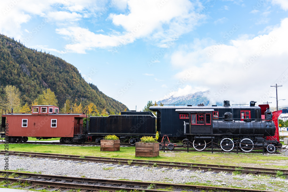 Naklejka premium Black steam engine/locomotive and red and black snow plow with caboose in public space on Skagway, Alaska