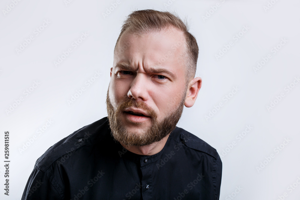 Fototapeta premium Unhappy blonde bearded man with discontent expression, frowns face, recieves bad news from interlocutor