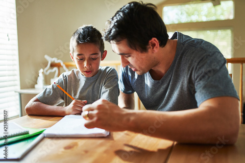father helping son with homework on table at home photo