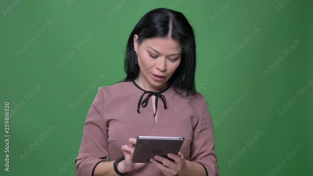 Closeup shoot of young attractive asian female with black hair using the tablet with background isolated on green Closeup shoot of young attractive asian female with black hair using the tablet with background isolated on green