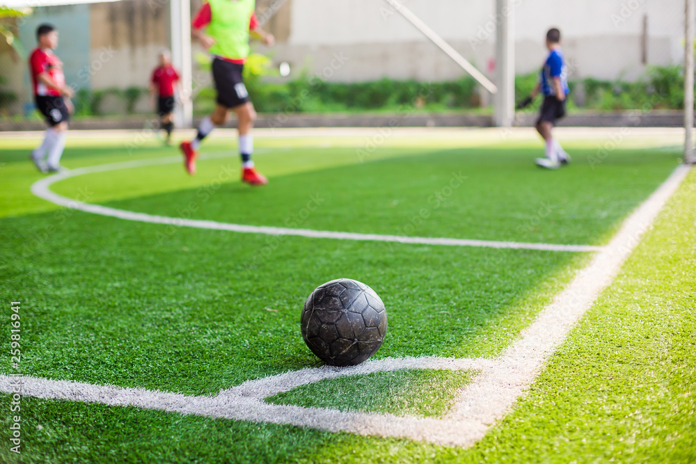 soccer ball on green artificial turf at corner of football field with blurry players background