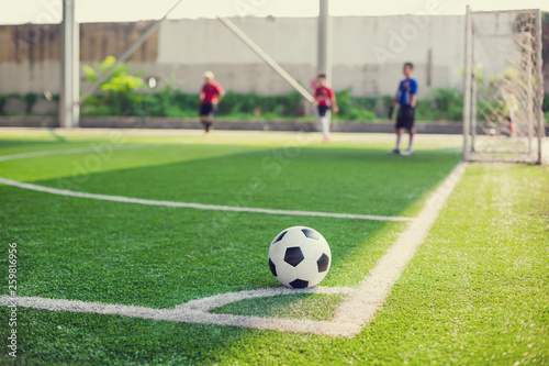 soccer ball on green artificial turf at corner of football field with blurry players background © Koonsiri