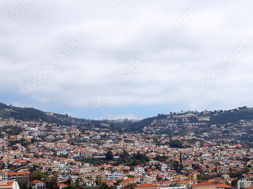 a wide panoramic view of the city of funchal in madeira with houses and tree covered hills under a cloudy sky