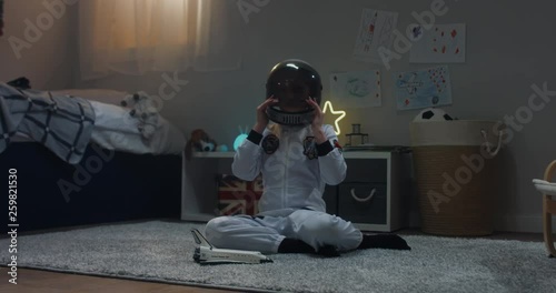 Cute little child girl wearing astronaut suit playing with toy shuttle space ship rocket at home, bedroom interior evening shot. 4K UHD RAW FOOTAGE