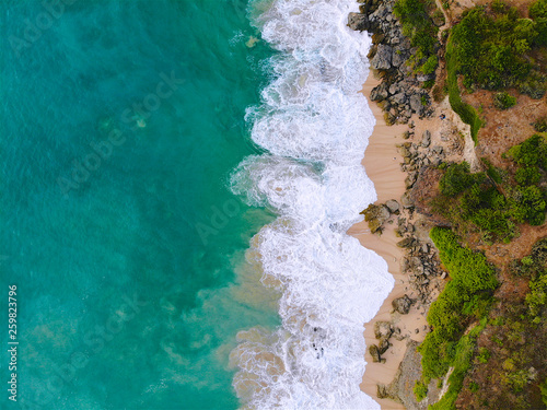 Aerial view sand beach with rocks and green cliff, top view of a beautiful sandy beach with rocks and waves, aerial shot with the blue waves rolling into the shore, some rocks present
