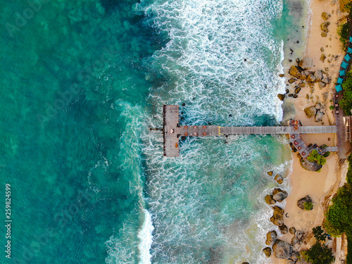 Aerial view of dock over tropical blue water and sand beach, with waves. Wooden pier in the sea. top drone view wooden jetty in blue water in Bali, Indonesia © Unwind
