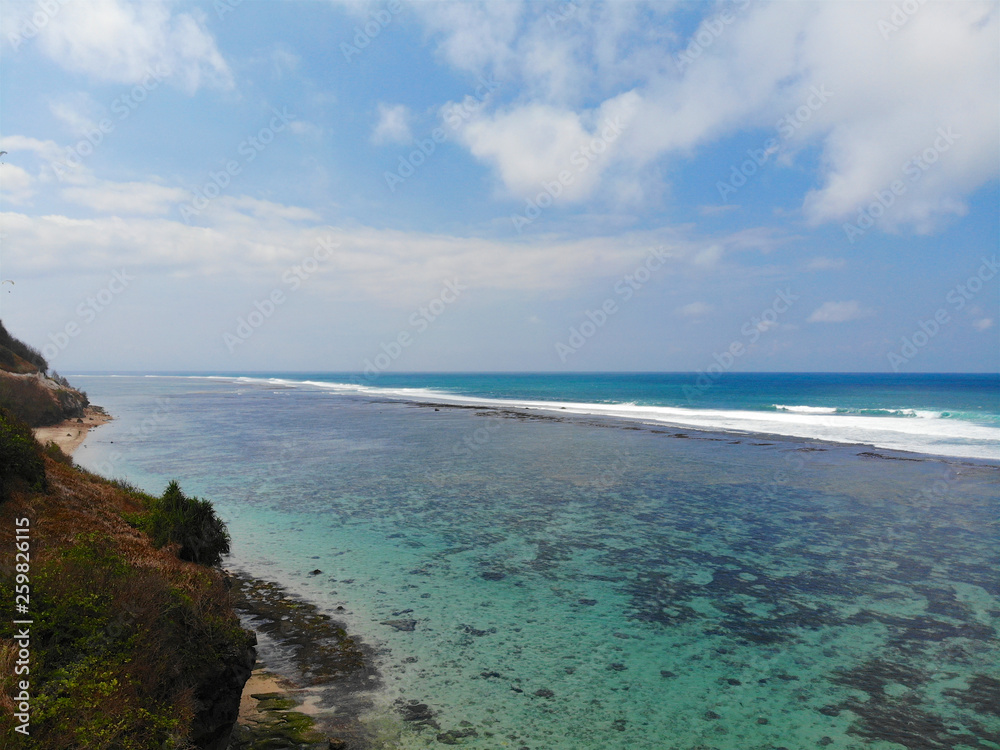 Aerial view of of the blue sea with rock cliff on sandy coastline. Beautiful turquoise sea water with waves for surfing in summer season in Bali. Beauty Indian ocean landscape, holiday destination