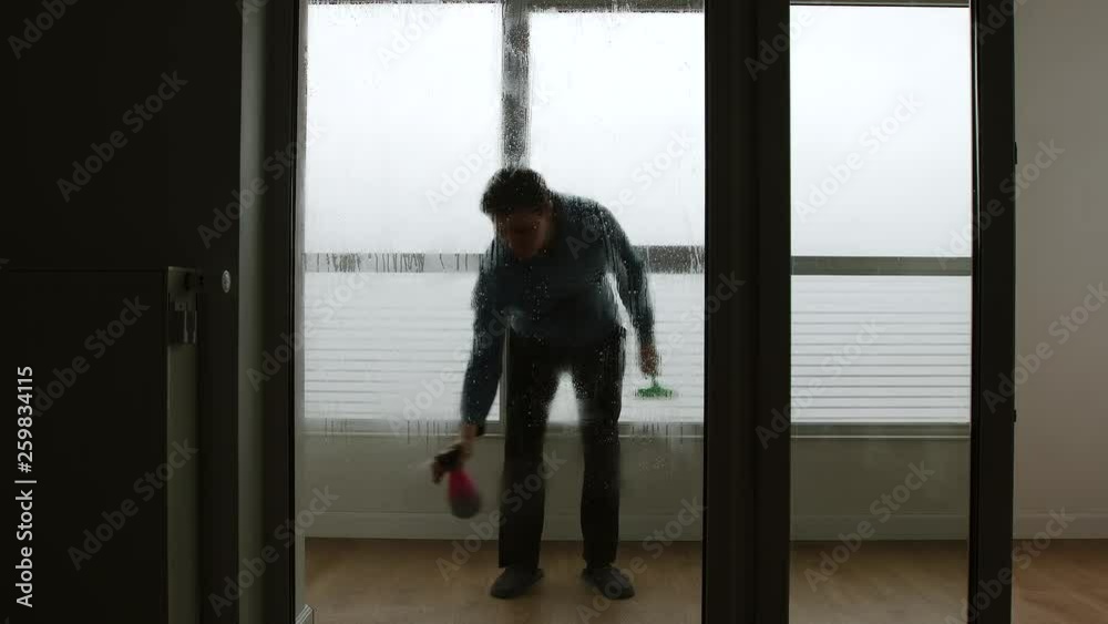 Man sprays window cleaner on large window and washes it indoors - Front View Man sprays window cleaner on large window and washes it indoors - Front View