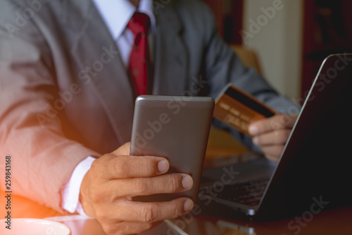  Businessman hand holding credit card and mobile smart phone for online shopping and payment with laptop computer on the desk. e business, ecommerce concept.