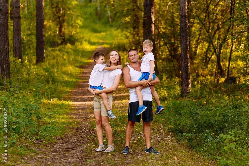 Fototapeta premium cheerful young parents hold two children in their arms in the summer outdoors. family