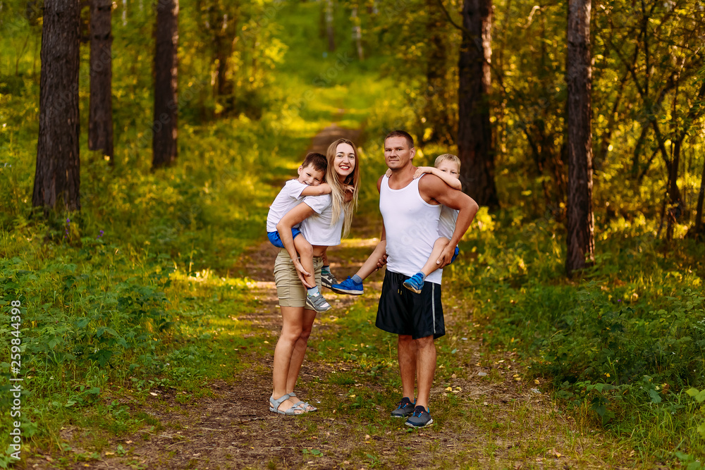 Fototapeta premium a cheerful young man and woman are holding two children on their backs in the summer outdoors. family