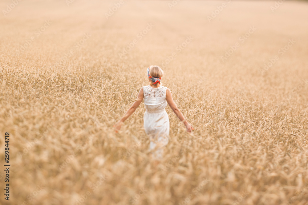 Young blonde woman standing on golden wheat field and touching wheat ears at sunny day. Enjoying nature. Beautiful girl in the rays of sunlight. Sunlight.