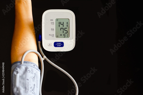 Woman take care for health,using sphygmomanometer to measure blood pressure,pulse and heart rate by self,isolated on dark background. Healthcare and hypertension concept. photo