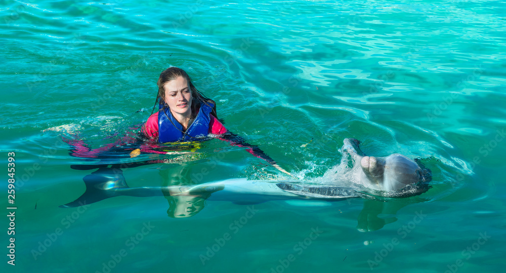 Fototapeta premium Smiling woman swimming with dolphin in blue water.