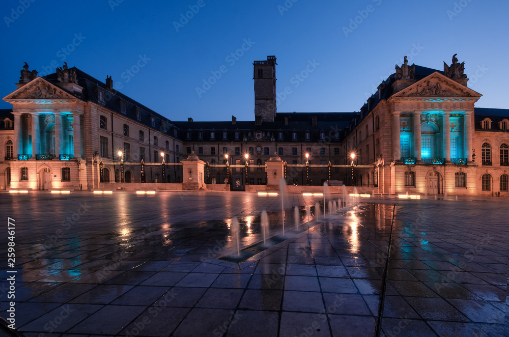 Palace of the Dukes of Burgundy at the hour of dawn. City of Dijon. France. In the foreground there is a fortan. The light of street lamps reflected on the wet pavement.