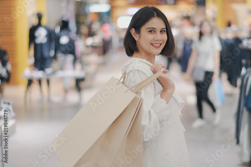 Young Asian beautiful woman shot hair smile and happy when shopping new clothes in a shopping mall store. Woman standing and holding a shopping bag in the store.