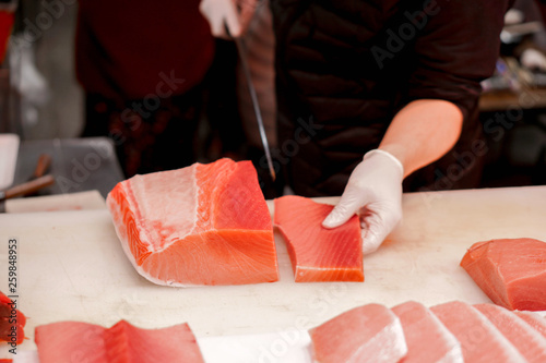 Hands of Japanese chef using chef knife sliced piece of fresh tuna fish for sell to customer in morning fish market, Japan.