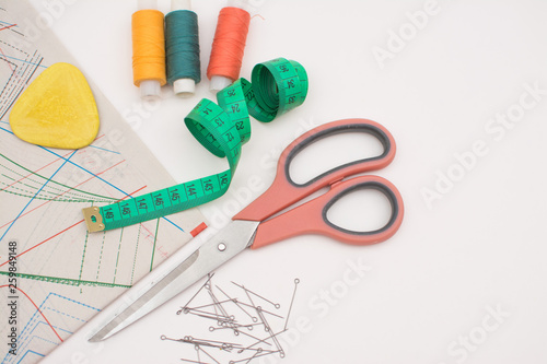 Sewing supplies for needlework, scissors, threads, needles, patterns, chalk, tape for measurement on a white background. View from above.