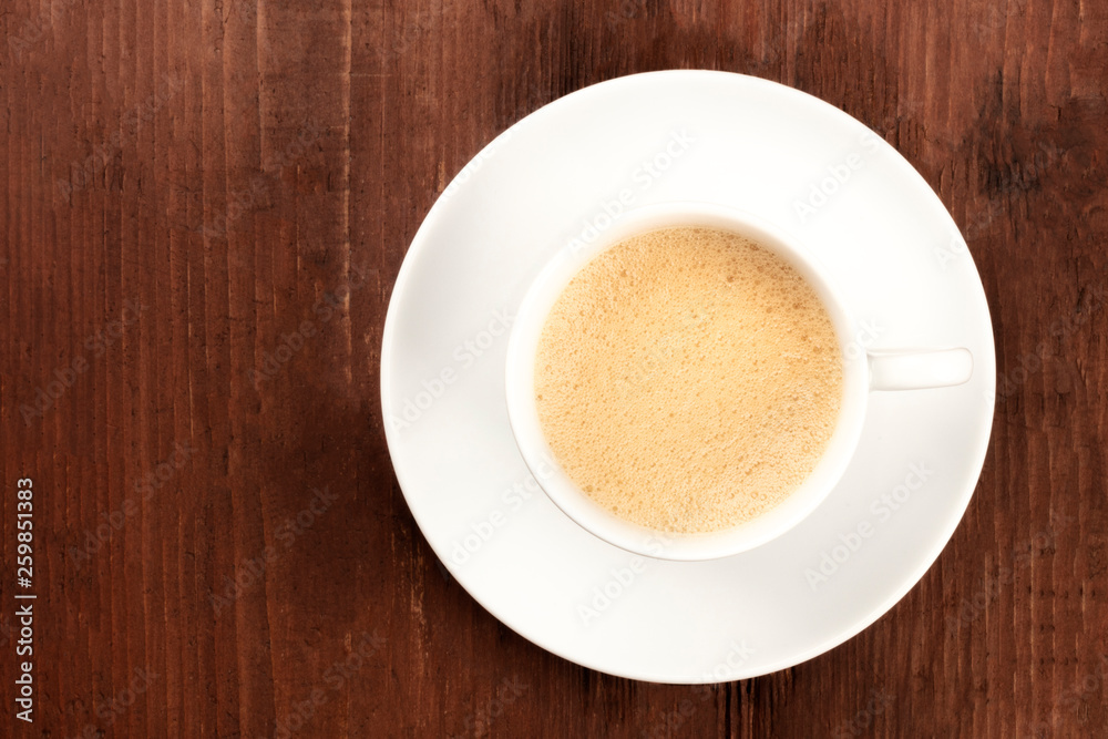 A cup of coffee with froth shot from the top on a dark rustic wooden background with a place for text A cup of coffee with froth shot from the top on a dark rustic wooden background with a place for text