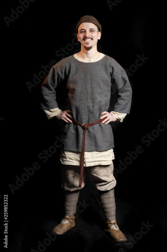 young man in casual gray clothes and a hat of the Viking Age (early Middle Ages) smiles © Volha