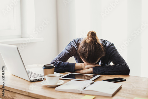 Tired and overworked business woman. Young exhausted girl sleeping on table during her work using laptop, digital tablet and smartphone. Entrepreneur, freelance worker or student in stress concept photo