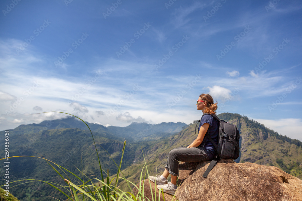 Happy young beautiful girl tourist with a backpack. Sit in the mountains and enjoy the view and nature.