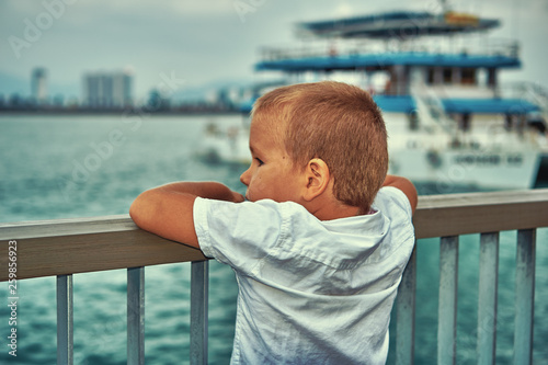 Young boy looking at the boat in the sea dreaming of becoming sailor