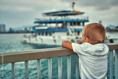 Young boy looking at the boat in the sea dreaming of becoming sailor