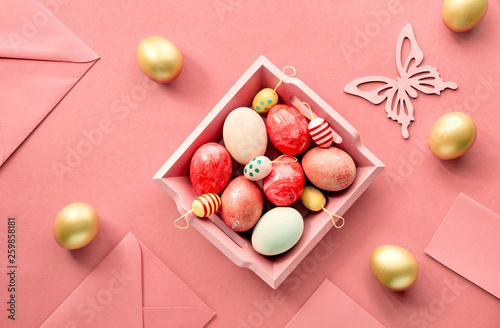 Easter flat lay on coral color paper with wooden tray full of decorative eggs, greeting cards, with envelopes and decorative flowes