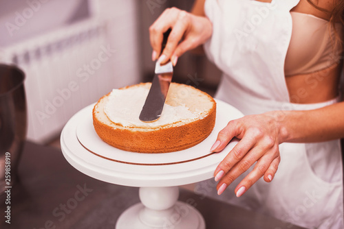Beautiful housewife in apron smears cream cake