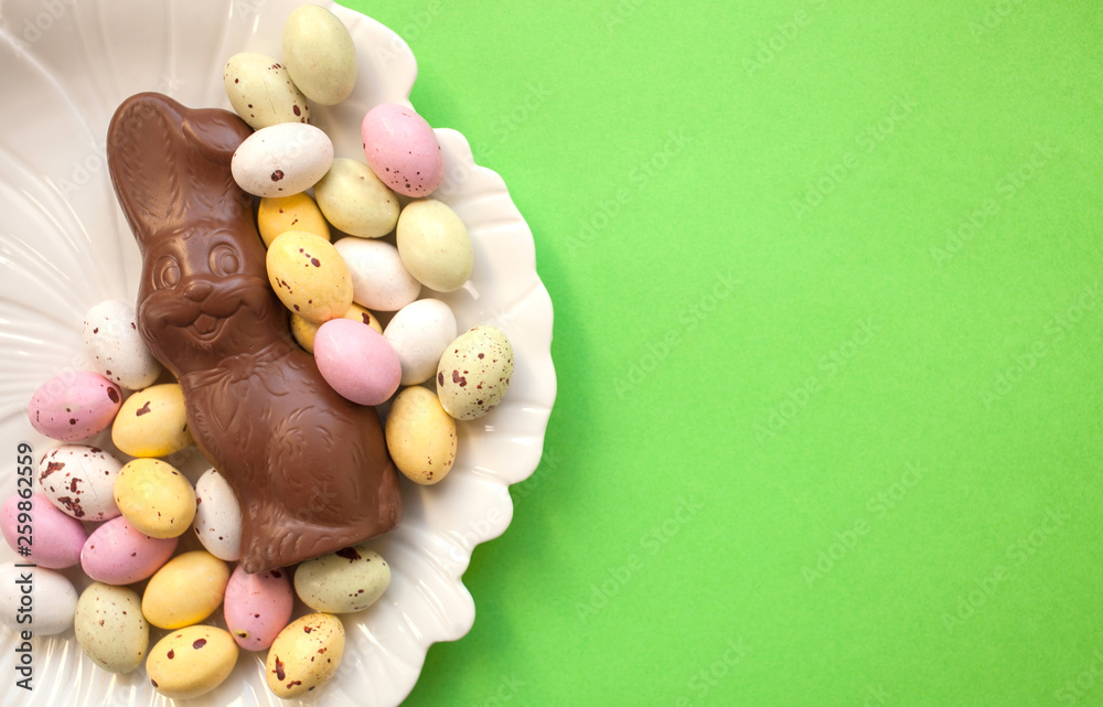 Easter bunny with colorful eggs on a white plate on a green background. top view copy space Easter bunny with colorful eggs on a white plate on a green background. top view copy space