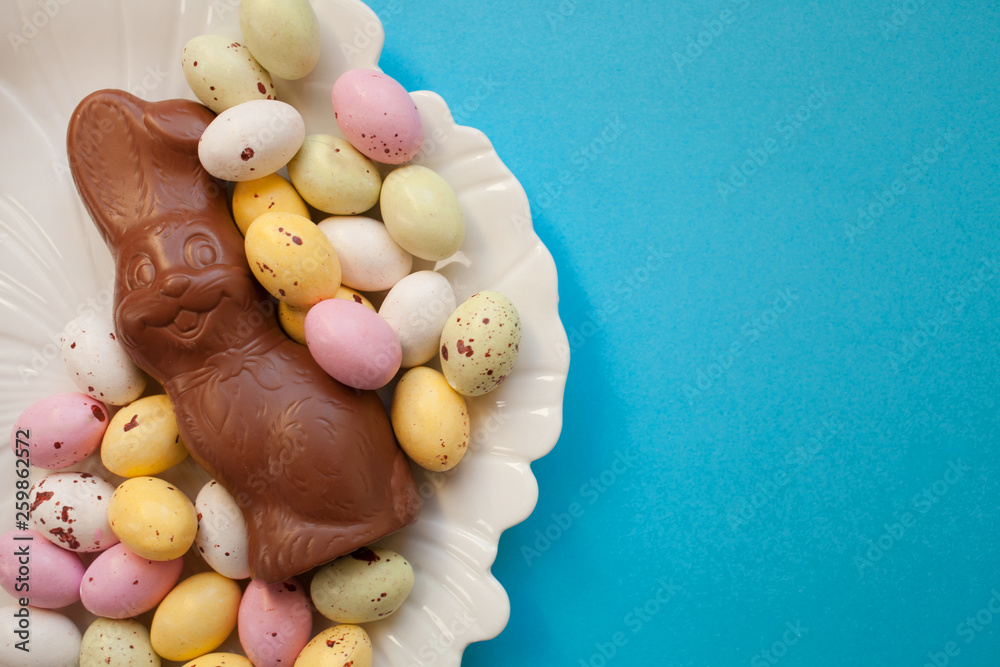 Easter chocolate bunny with small colorful eggs on a plate on a blue background. top view copy space Easter chocolate bunny with small colorful eggs on a plate on a blue background. top view copy space